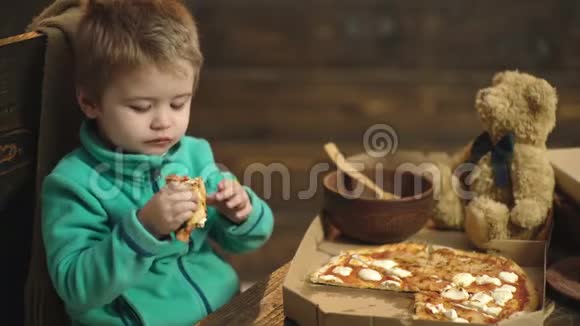 在木制背景下吃披萨的男孩美味的披萨小男孩在吃披萨饥饿的孩子咬一口视频的预览图