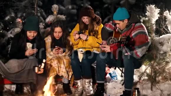一群年轻人在冬林中坐在火边人们坐在手机里微笑社会视频的预览图