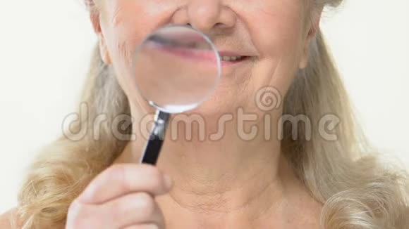 老年女性用放大镜在皱纹老脸上抗龄化妆品视频的预览图