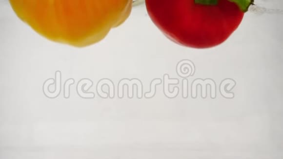 两个红辣椒和黄辣椒掉进水里白色背景上有飞溅和气泡视频的预览图
