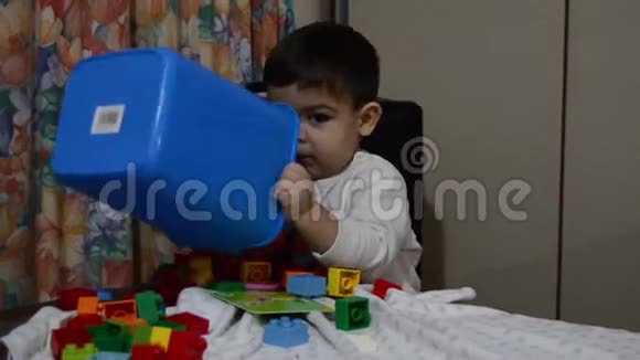 一个半岁的男婴把桌上放着乐高积木的蓝色垃圾箱倒空视频的预览图