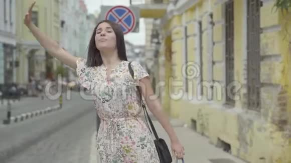 穿着夏装手里拿着购物袋试图在一位老人的街道上搭出租车的无忧无虑的年轻女子视频的预览图