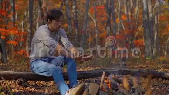 年轻人坐在寒冷的秋林中的篝火旁秋假概念视频的预览图