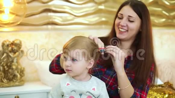 年轻的母亲在节日装饰的家里为年幼的女儿做发型视频的预览图