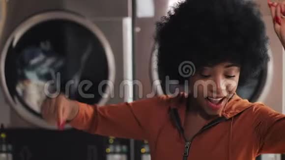 年轻微笑的非洲裔美国妇女在自助洗衣店滑稽跳舞的肖像视频的预览图