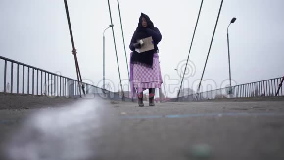 成年无家可归的妇女住在河港附近的桥上天气寒冷多风灰色请求帮助和乞求金钱视频的预览图