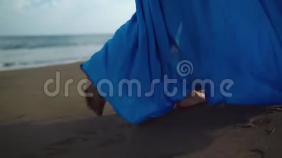 穿着漂亮蓝色裙子的女人沿着黑色的火山海滩散步慢动作视频的预览图