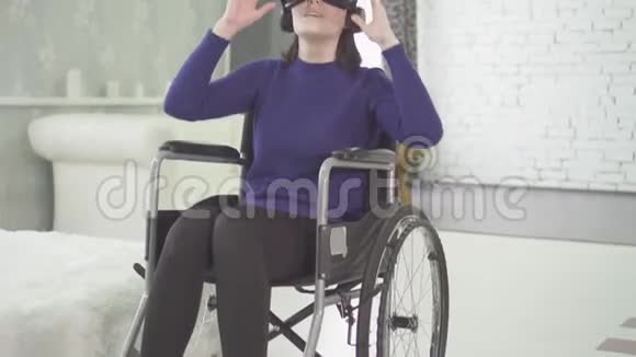 年轻漂亮的残疾妇女在家坐轮椅使用3d技术vr头盔视频的预览图