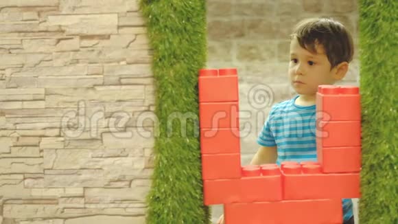 男孩三岁独自在孩子们房间里玩耍站着一堵大塑料块的墙视频的预览图