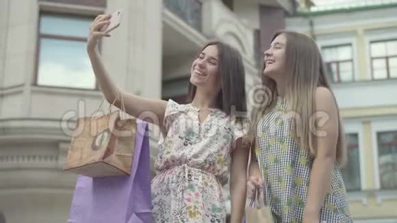 两个快乐的女朋友购物后带着购物袋在户外手机上自拍快乐女孩的休闲视频的预览图