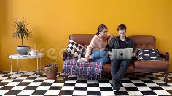 漂亮的年轻夫妇坐在沙发上的笔记本电脑上库存录像几个学生一起看视频的预览图