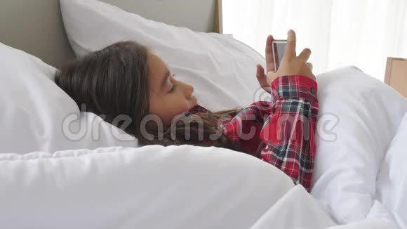 可爱的女孩躺在床上看着智能手机和社交媒体娱乐人们的生活方式和教育儿童和儿童视频的预览图