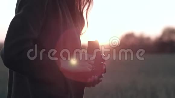 女性站在田野上带着老式相机在背景夕阳下带着阳光视频的预览图