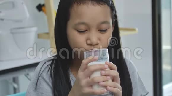 儿童亚洲女孩喝一些牛奶在桌子上舒适的儿童在家的概念视频的预览图