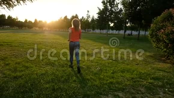 运动女孩在城市公园日落时慢跑穿过草地慢动作视频的预览图