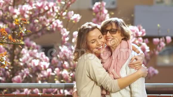 成熟的母女拥抱祝贺母亲节美丽的春日盛开的玉兰视频的预览图