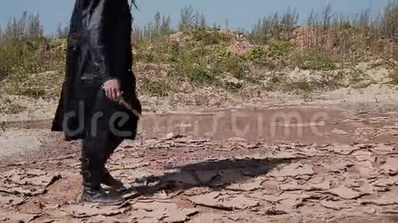 穿着黑色斗篷和帽子的探路者在沙漠中的裂缝地面上视频的预览图