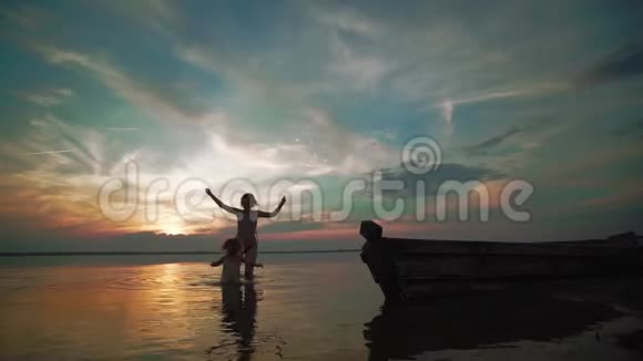 慢动作日落时分一个女人和一个小孩在湖面上欢快地奔跑小孩子的剪影视频的预览图