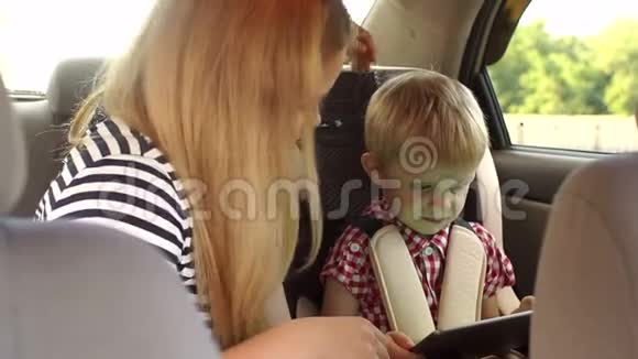 一位有爱心的母亲坐在车里的孩子旁边他们玩平板电脑视频的预览图
