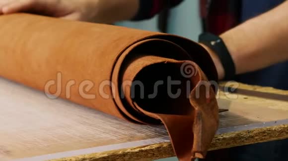 一个制革工在桌子上展开一卷皮革皮革大师选择扭曲的皮革关门视频的预览图