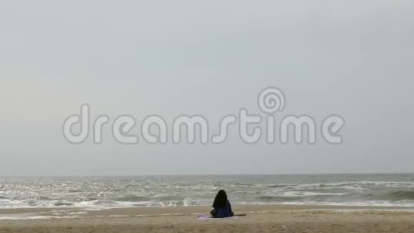 女孩独自坐在海边的沙滩上看着海浪视频的预览图