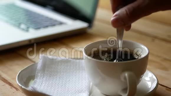 咖啡杯中的热黑咖啡在背景下用电脑笔记本搅拌视频的预览图