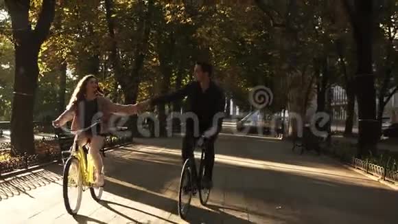 夏天美丽的年轻夫妇骑着自行车在空荡荡的城市公园或林荫大道上把手举起来视频的预览图