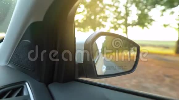 汽车在日落时穿过被树木包围的道路时从后视镜中观看视频的预览图