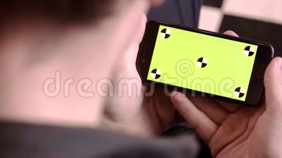 特写男人拿着绿色屏幕的手机库存录像男人拿着新智能手机看着绿色屏幕视频的预览图