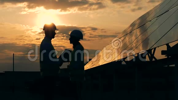 工人在日落背景下靠近太阳板交谈侧视视频的预览图