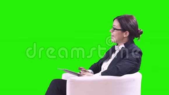 商务女性坐在绿色背景的扶手椅上在平板电脑上工作采访和微笑4k视频的预览图
