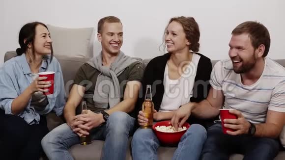 年轻的女性和男性的朋友都喜欢喝饮料他们坐在家里的沙发上吃红碗里的爆米花视频的预览图