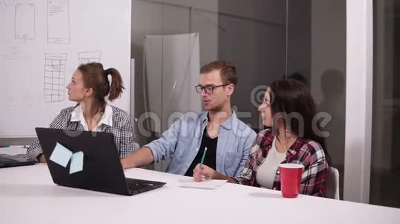 戴着眼镜的年轻人和两个女人在办公室桌上创造性地坐在一起讨论一些事情视频的预览图