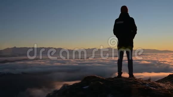 一个人的剪影站在云层上方的处凝视着夕阳宁静的概念视频的预览图