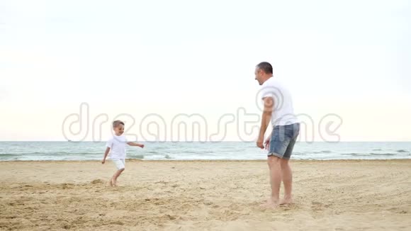 一个快乐的小男孩沿着沙滩跑向他的父亲快乐的爸爸和孩子玩把他抱在怀里视频的预览图