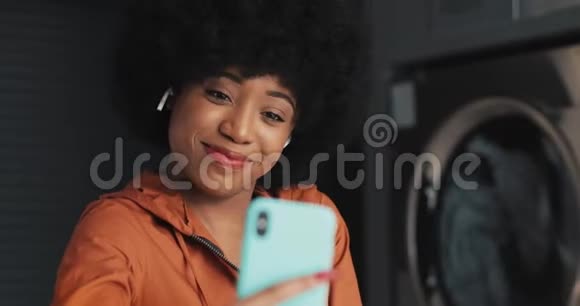 快乐迷人的非裔美国年轻女子在自助洗衣店视频聊天自助公共洗衣店视频的预览图