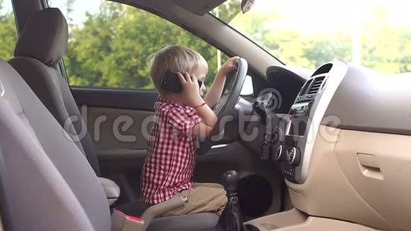 一个有趣的小男孩坐在一辆车的轮子后面打电话视频的预览图
