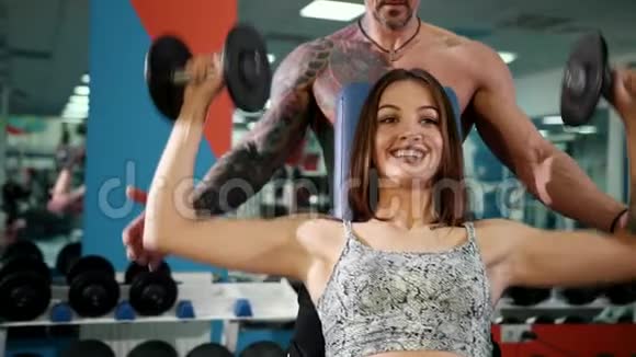 漂亮的女人和一个在健身房举起哑铃的野蛮男人漂亮的女人在健身房和丈夫一起举起哑铃视频的预览图