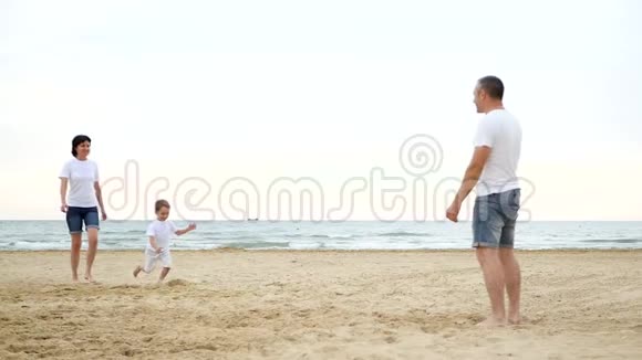 幸福的家庭在沙滩上休息快乐的微笑男孩向他父亲跑去爸爸在玩耍他的孩子在长大视频的预览图