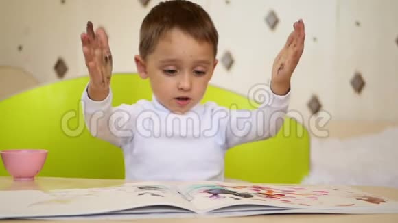 快乐的男孩用手在纸上画画淘气的孩子把手拍在油漆上教育视频的预览图