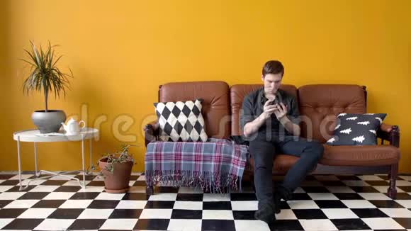 坐在沙发上打电话的家伙库存录像年轻人热情地打电话坐在时髦的地方视频的预览图