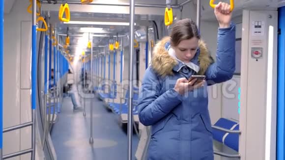 女人坐在一辆空的地铁车里在她的智能手机上浏览站立并握住扶手视频的预览图
