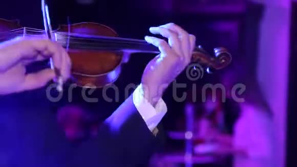 特写男音乐家拉小提琴在黑暗的背景与彩色的灯光视频的预览图