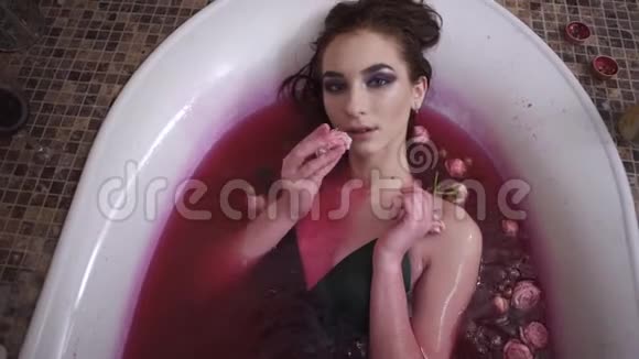 可爱的年轻女人在水疗中心用玫瑰洗澡漂亮的女孩慢慢地把玫瑰放进嘴里抬头看着镜头可爱视频的预览图