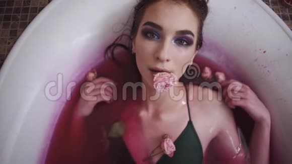 一幅美丽的女人拿着玫瑰在嘴里用花洗澡的肖像性感的女孩从嘴里掉了一朵玫瑰视频的预览图
