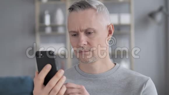悲伤的白发人在智能手机上失去在线视频的预览图