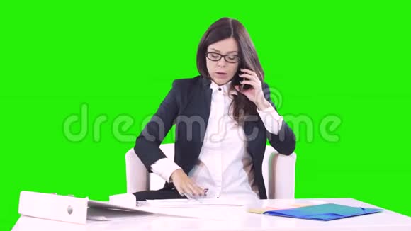 年轻的深色头发的年轻女人坐在办公室的办公桌后面打电话桌子上有文件视频的预览图