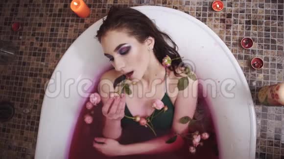 可爱的女人在水疗中心用玫瑰洗澡漂亮的女士慢慢地把玫瑰放进嘴里抬头看着镜头可爱的女孩视频的预览图