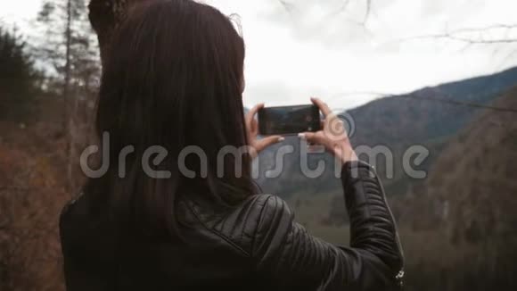 年轻女子在智能手机摄像头上拍摄山河景观照片通过网络社交媒体分享视频的预览图