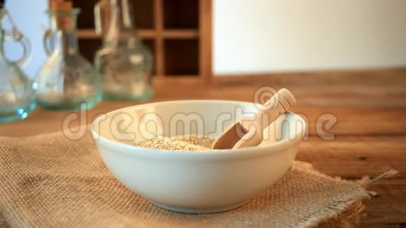 女人的手正在倒干藜麦颗粒在木制厨房桌子上有勺子视频的预览图